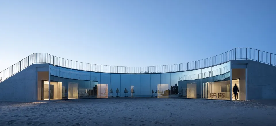 A modern beach house with glass and concrete exterior on a sandy beach.