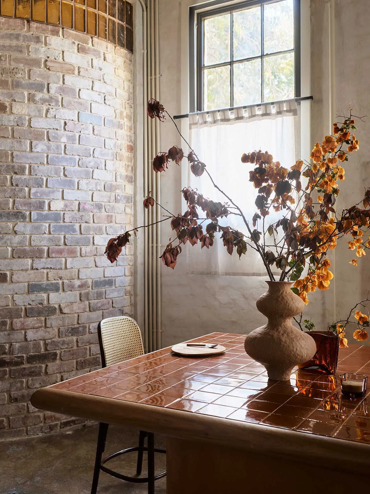 A modern, industrial-style interior with concrete and brick surfaces, a tile table, and a decorative plant vase.