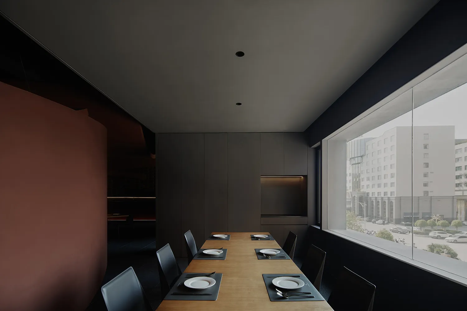 Modern restaurant dining room with black interiors, wooden tables, and white plates on placemats.