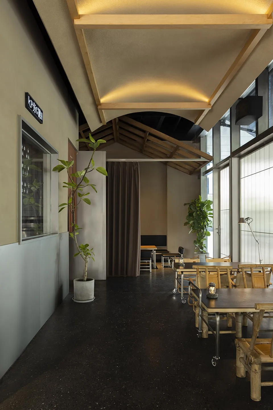 A restaurant interior featuring wood and concrete materials with large windows and industrial-style lighting.