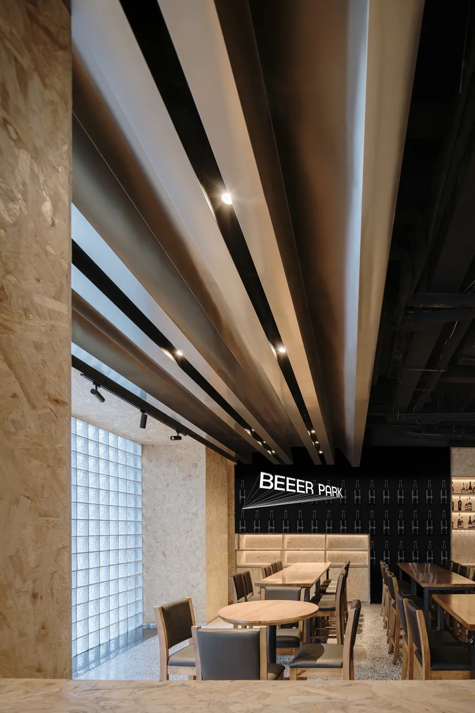 A modern industrial restaurant interior with a metal beam ceiling, wooden tables, and sleek black accents.