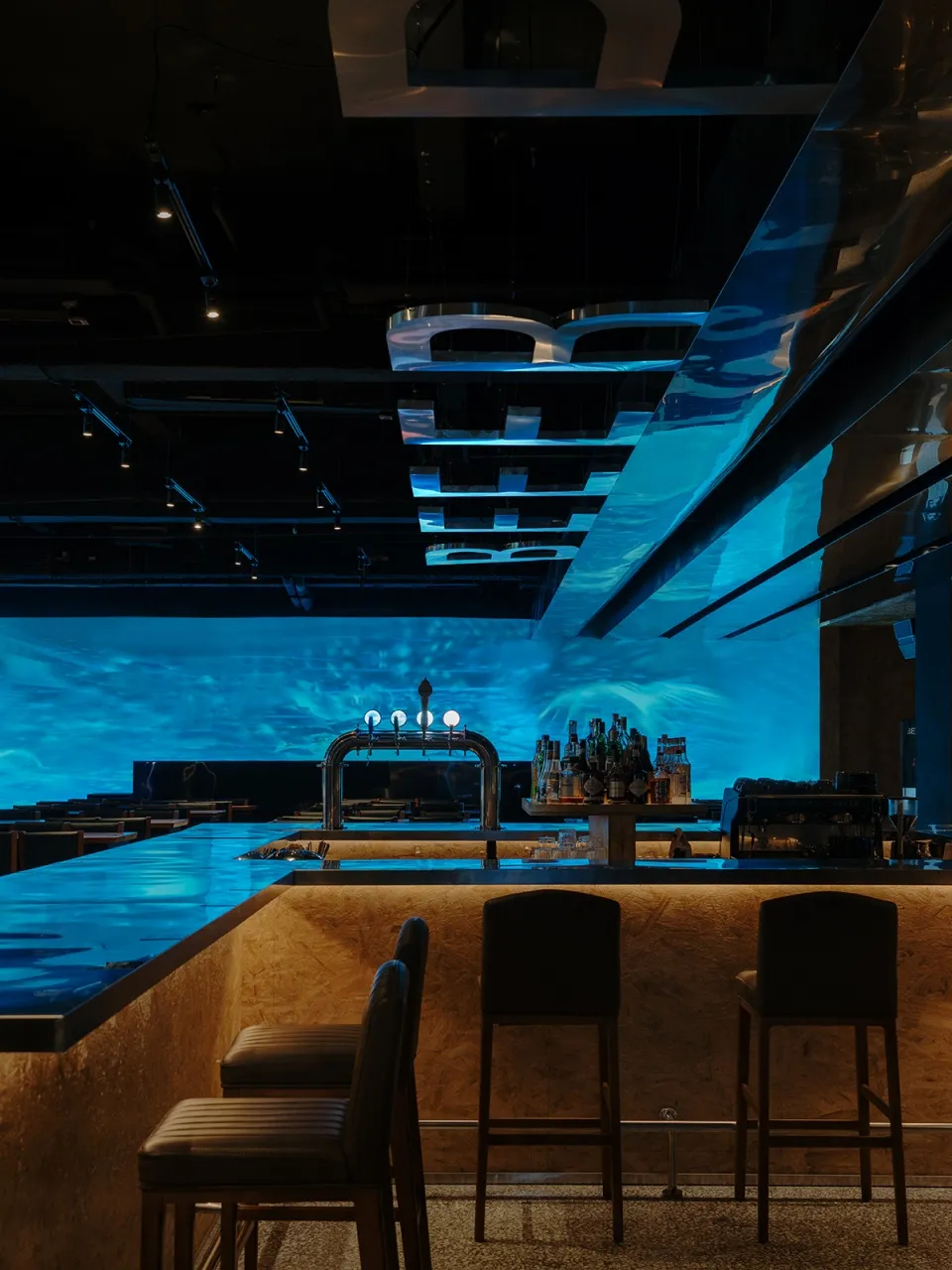 Modern bar with an underwater-themed design featuring metallic elements and glass.