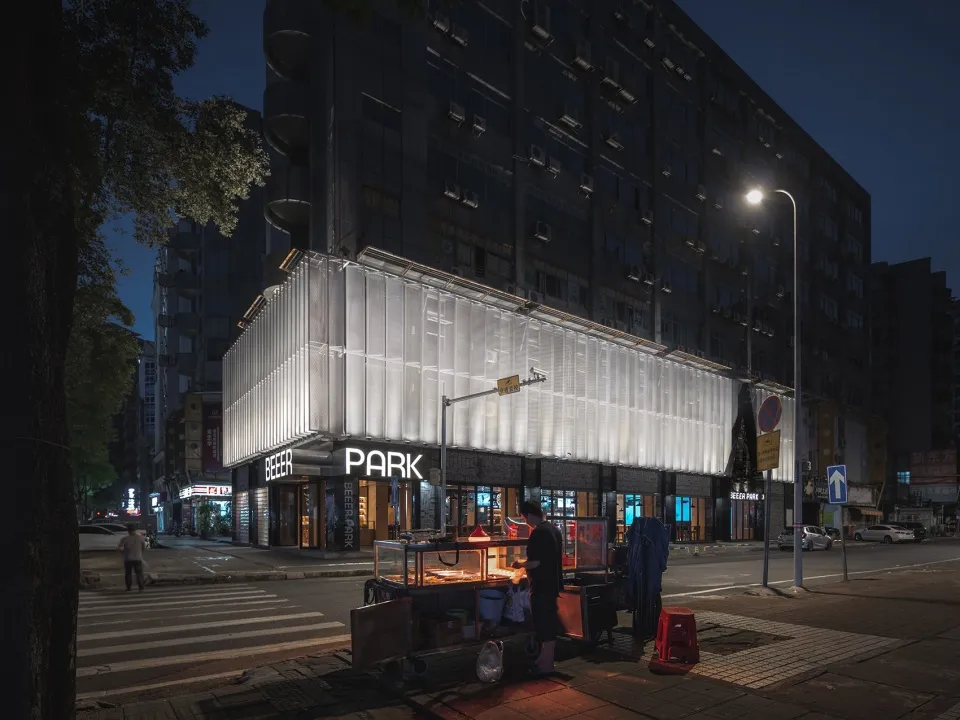 A street corner storefront with illuminated bonded glass panels and a food cart at night.