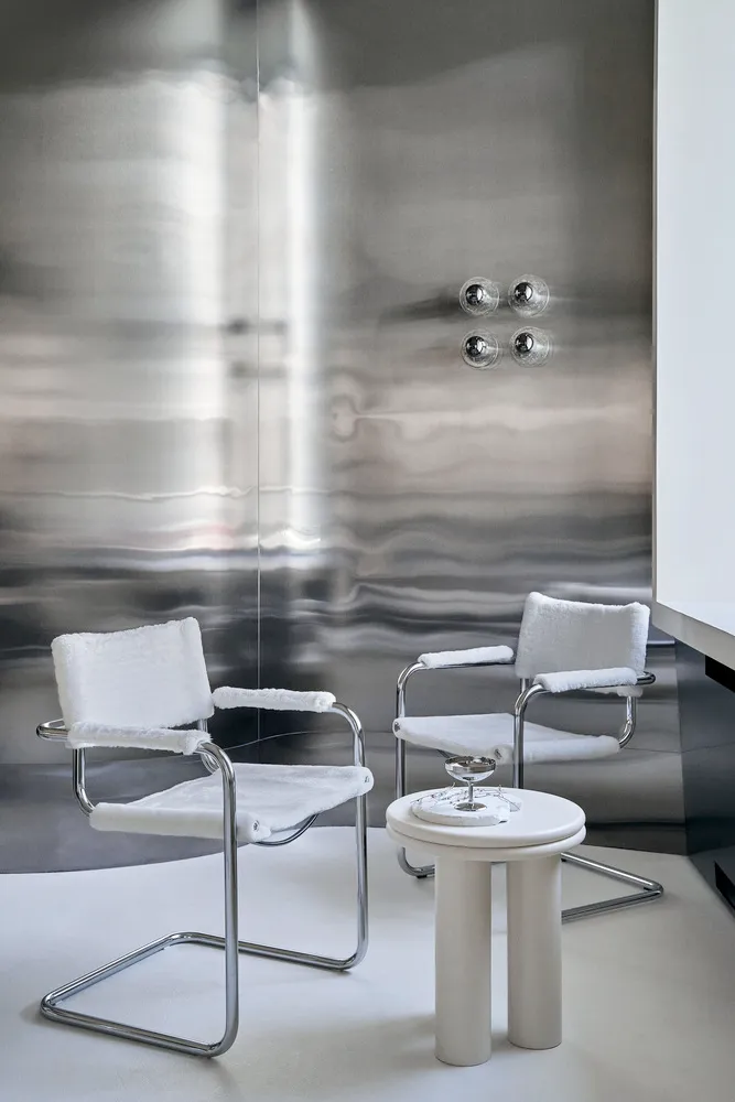Minimalist modern interior design featuring a sleek glass table and chairs against a metallic wall.