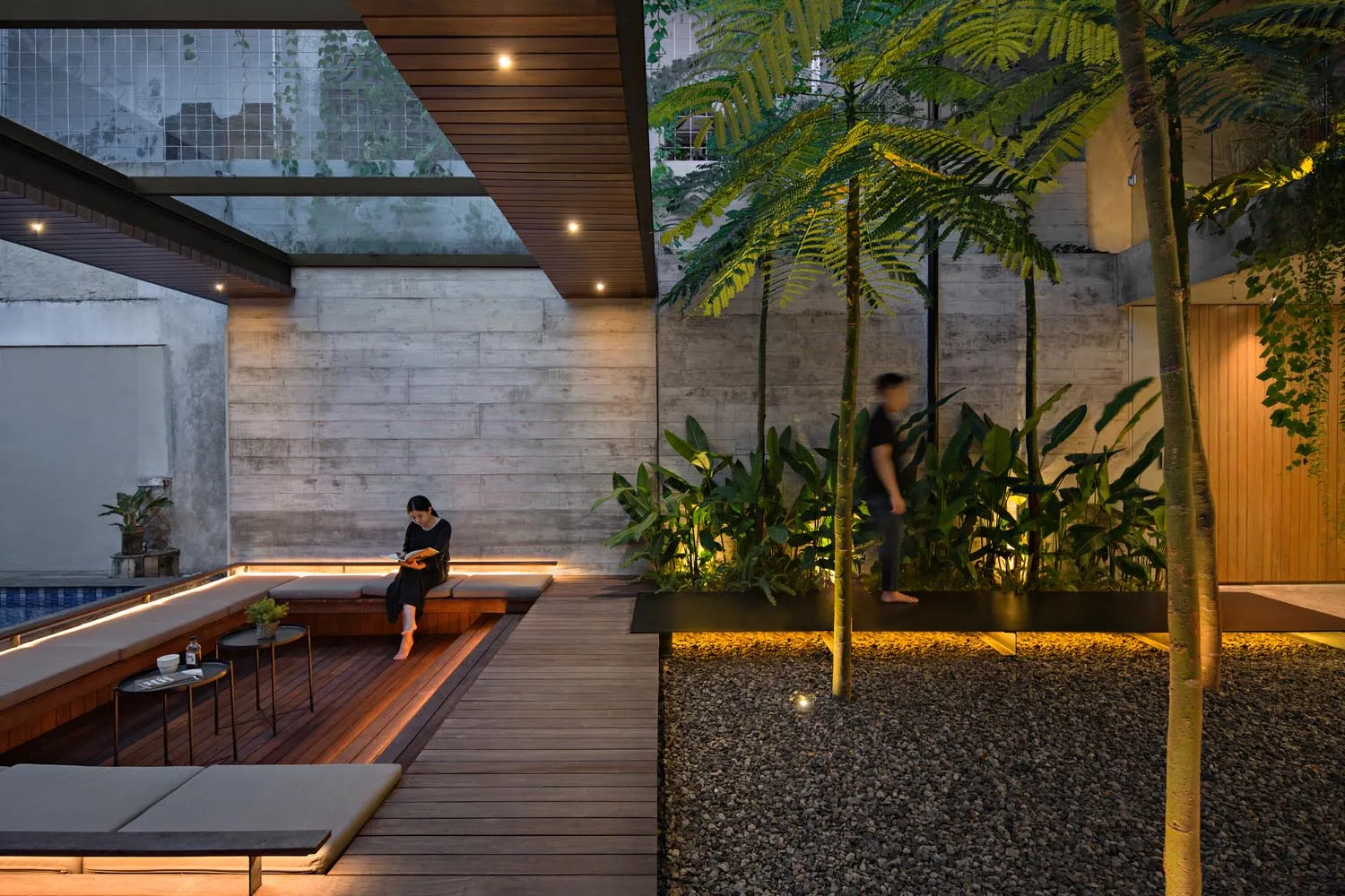 A modern residential patio featuring wooden decks, concrete walls, and lush green plants.