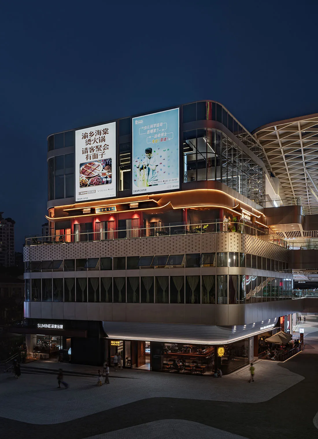 Modern shopping center with glass facade at night with illuminated advertisements.