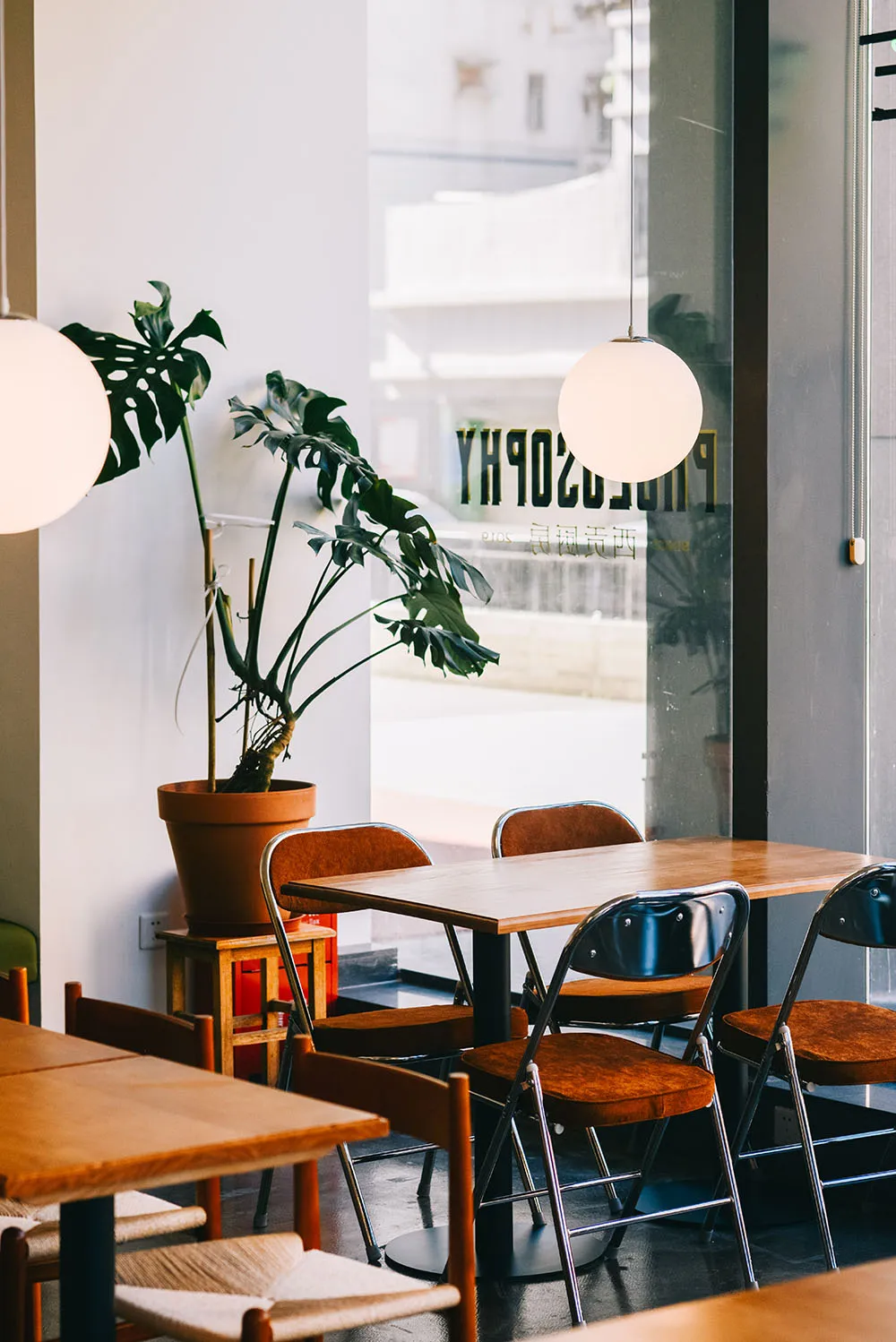 Modern cafe restaurant with wooden tables, metal chairs, glass windows, and green plant