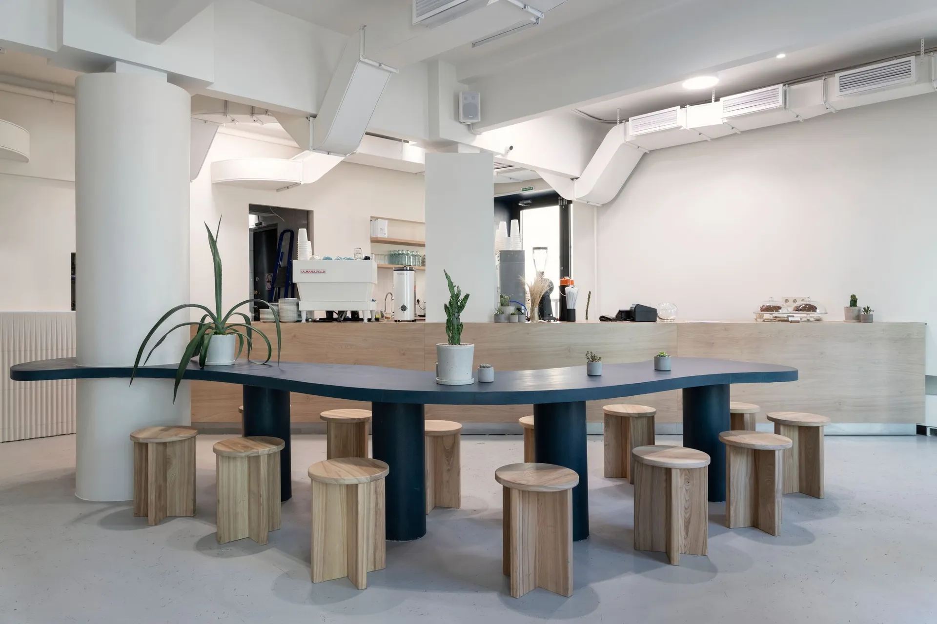 A modern, industrial restaurant interior with concrete accents and a large communal table.