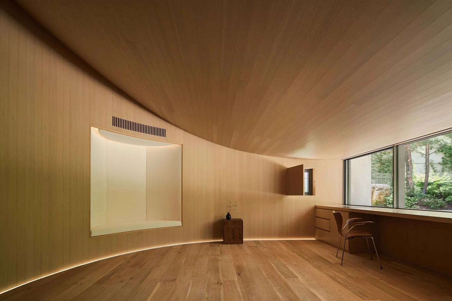 A minimalist residential interior with wood walls and ceiling, featuring a desk and window.