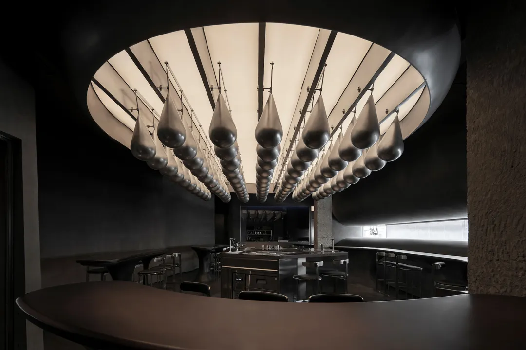 A modern restaurant bar with a curved countertop and hanging silicone drop lights.
