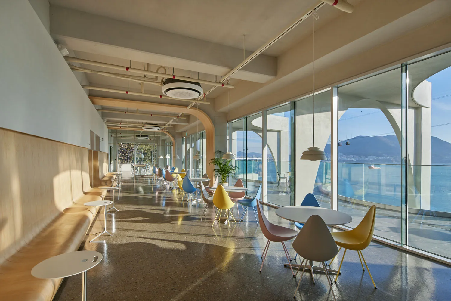 Industrial-themed coffee shop with steel furniture and large windows overlooking a scenic view of mountains and water.
