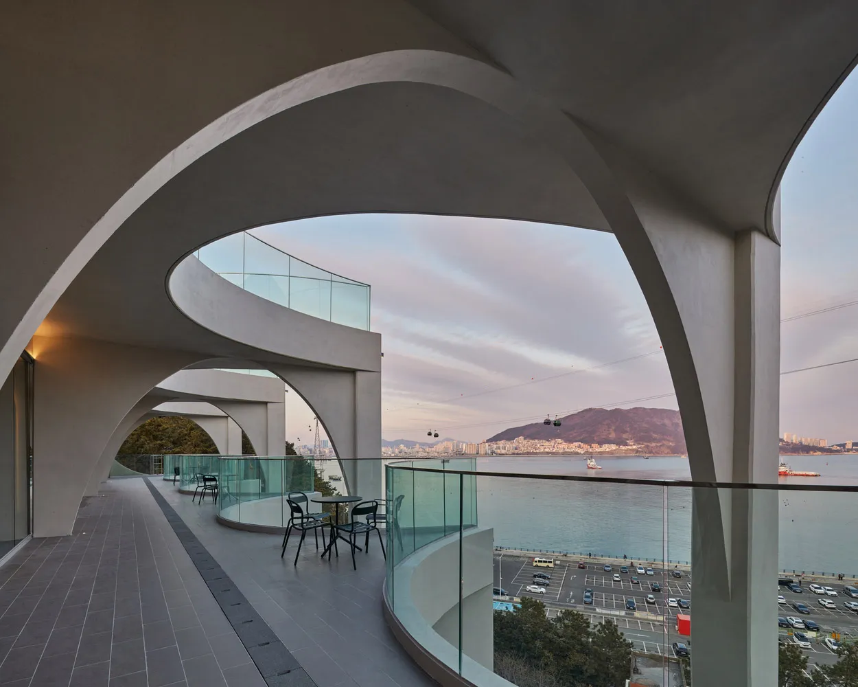 Modern balcony with glass railings showcasing a view of the sea and mountains in the background.