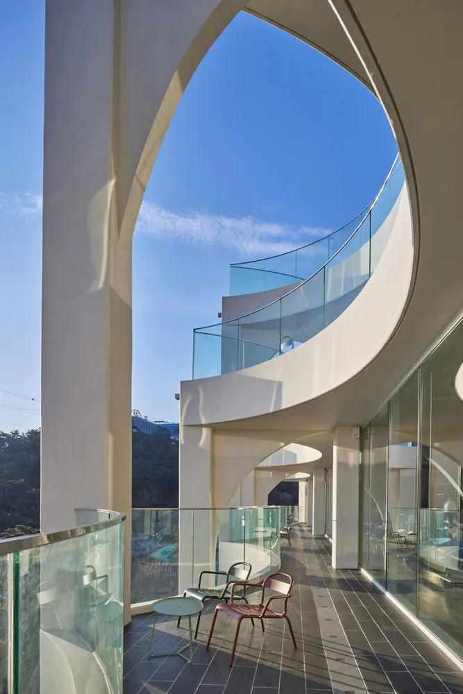 Modern residential balcony featuring glass railings and concrete pillars, set against a clear blue sky.