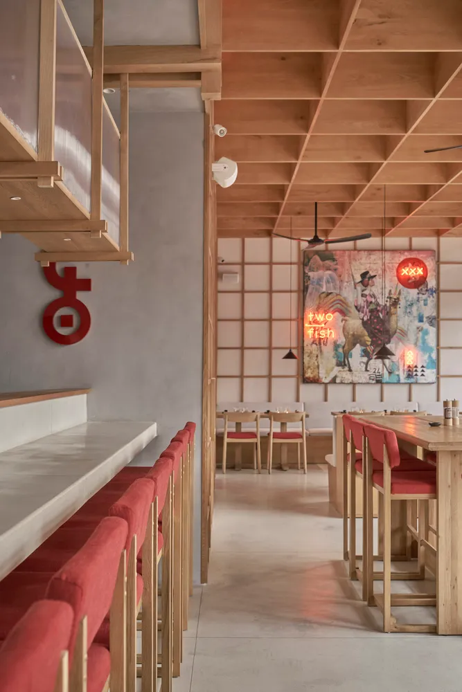 Modern restaurant interior featuring wooden tables, red cushioned seating, and a mural with two fish.