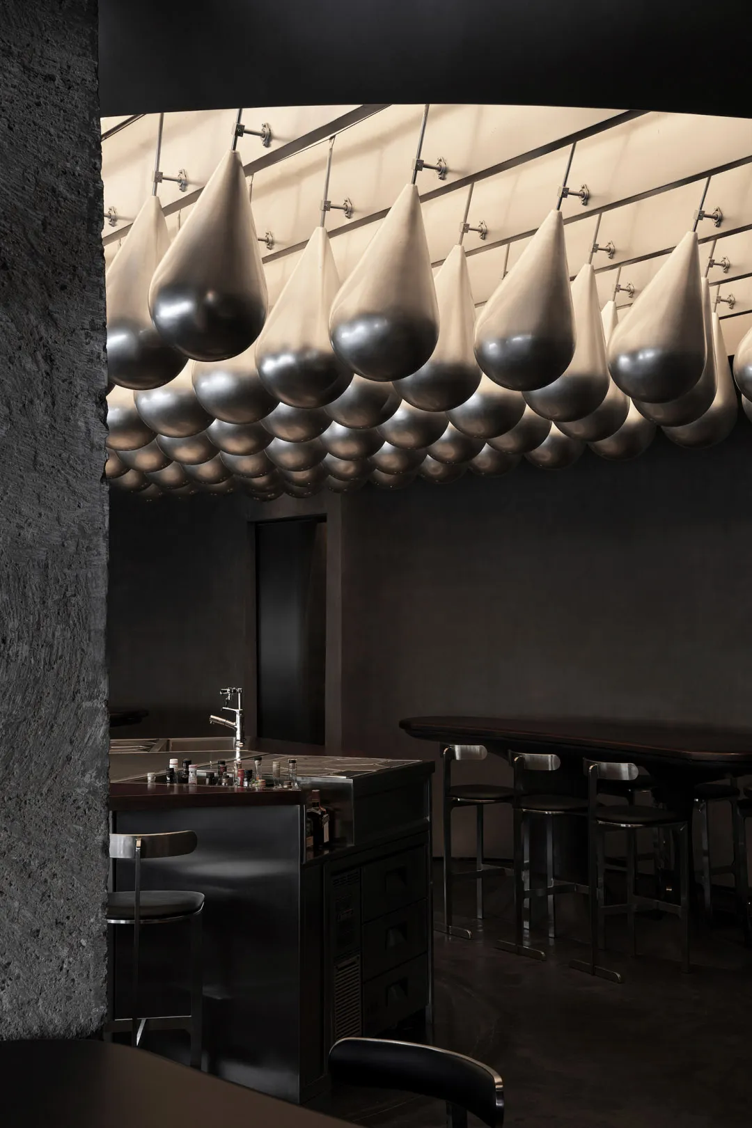 An interior of a modern restaurant with hanging metallic pendant lights and a black color scheme.