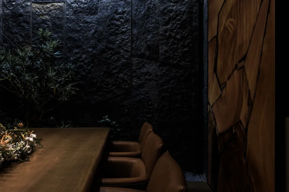 Industrial style restaurant interior with black stone walls, wooden table, and leather chairs.