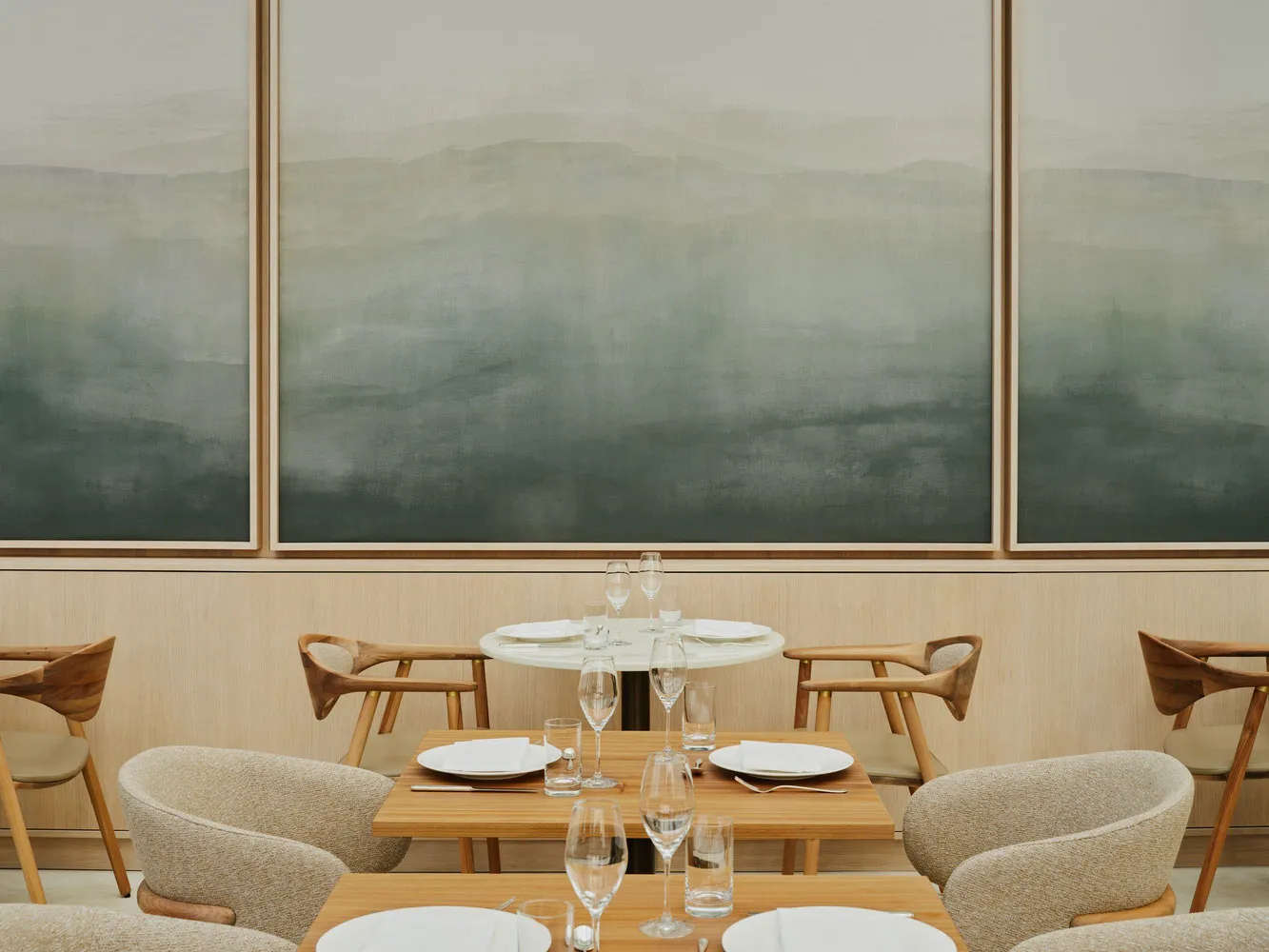 A minimalist restaurant interior with wooden tables, chairs, and abstract wall art.
