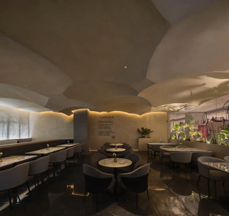 A modern restaurant interior with concrete walls, glass partitions, and white lighting fixtures.