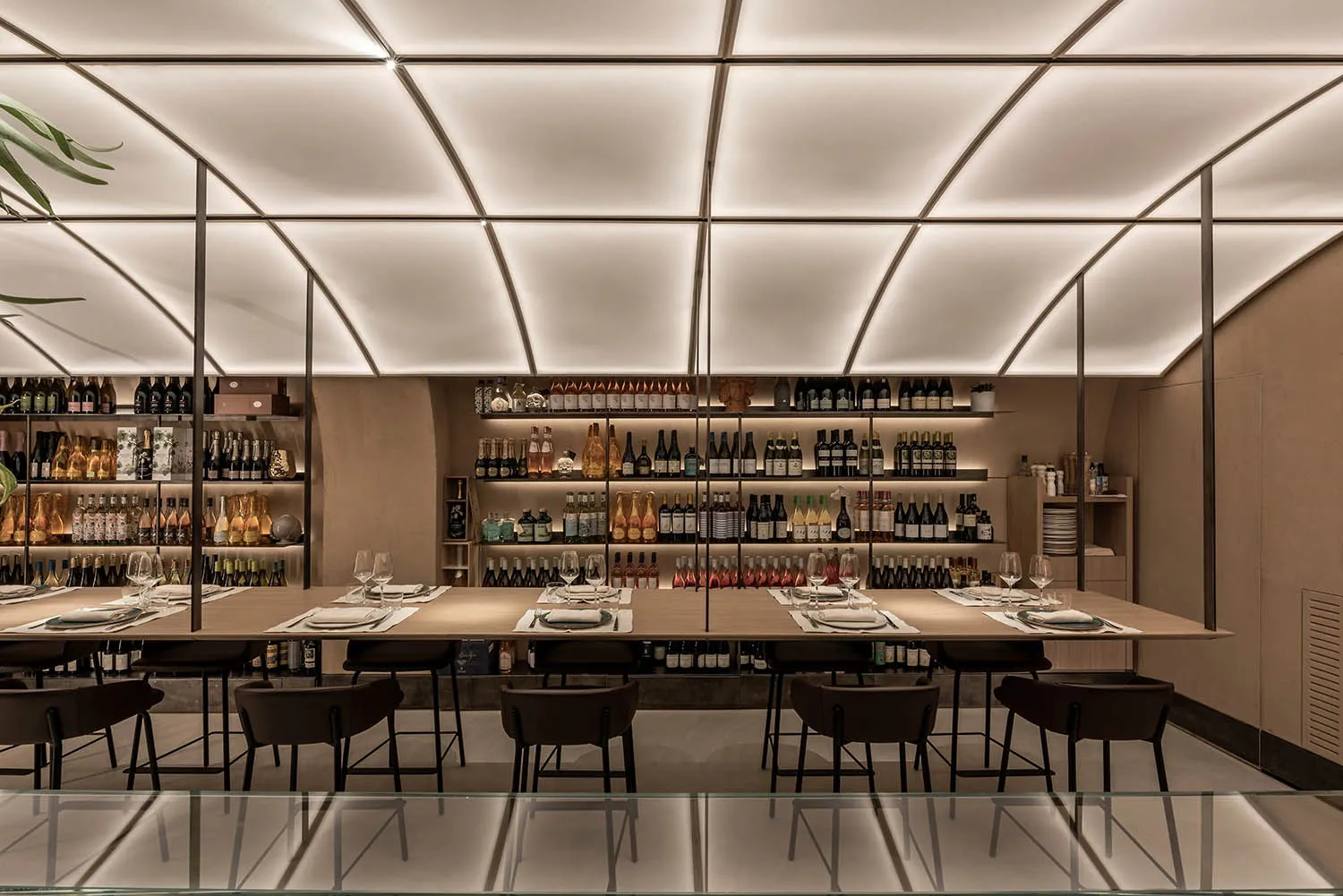 A spacious and contemporary restaurant interior featuring a large dining table surrounded by chairs and a well-stocked wine b