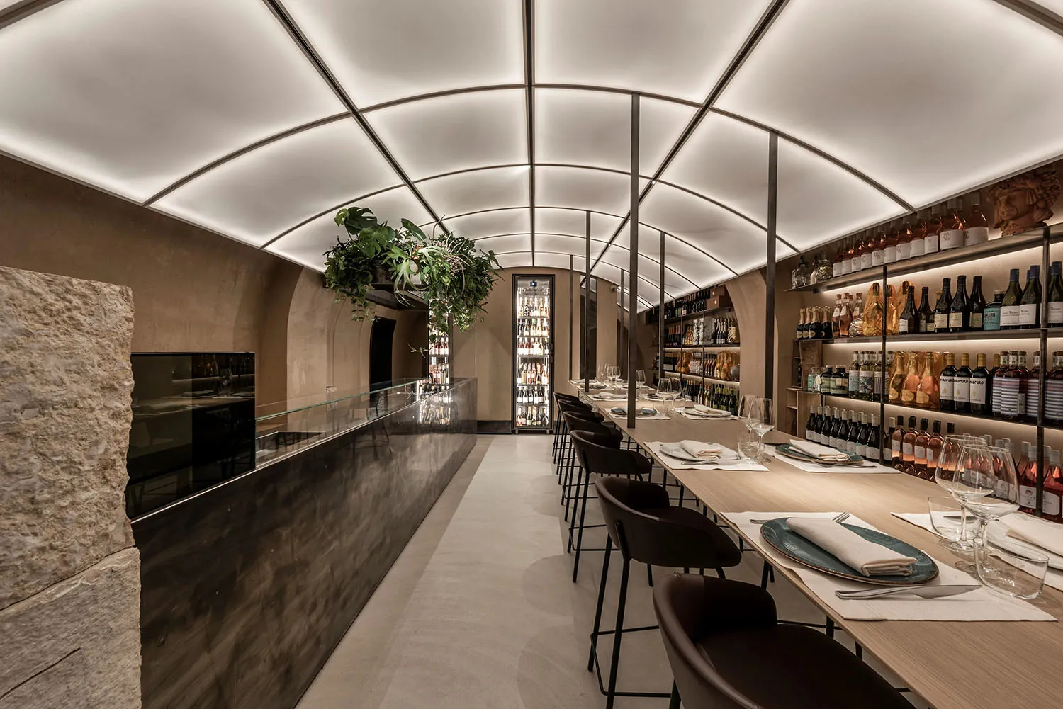 A modern wine bar with concrete countertops, wood shelves, and glass bottles of wine.
