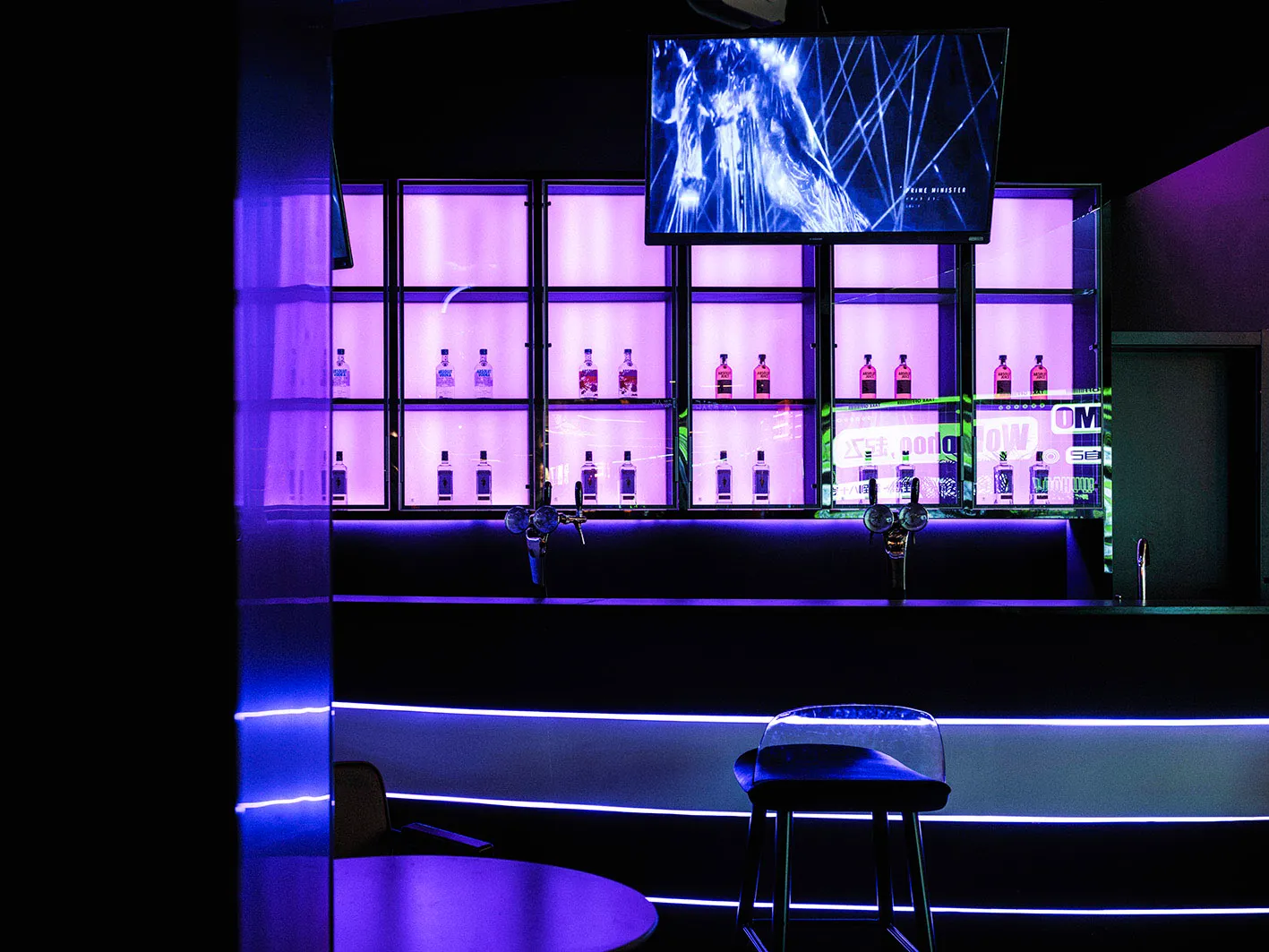 Modern bar interior with purple LED lights and illuminated shelving displaying bottles of alcohol.