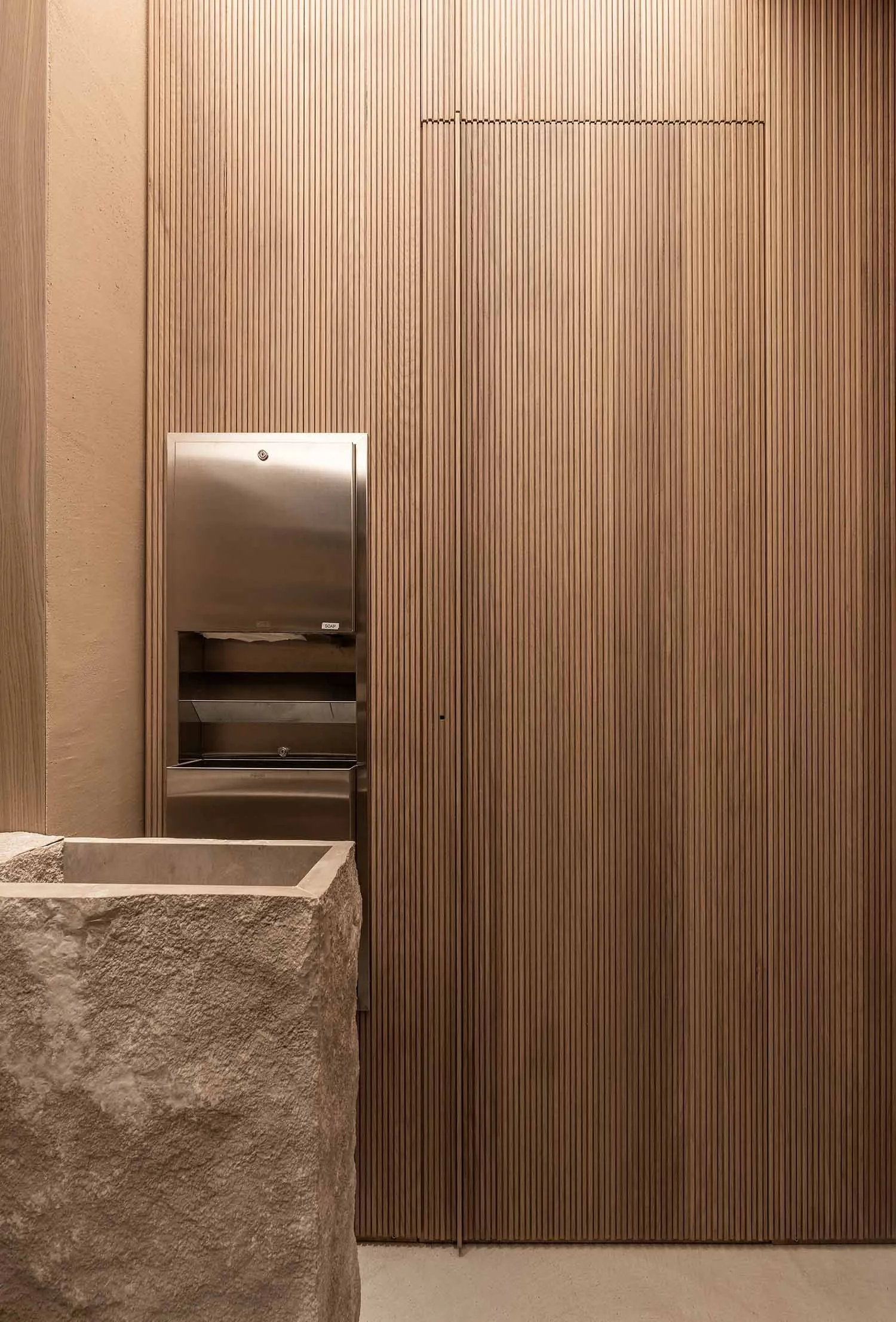 A modern interior featuring a wooden panel wall and a stone sink, emphasizing contemporary design elements.