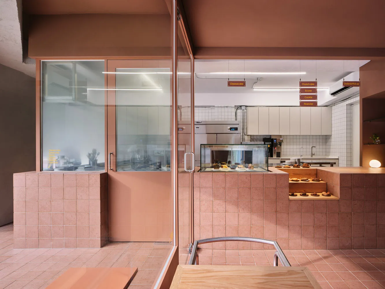 Contemporary cafe interior featuring a terracotta-tile half-wall with a display case showcasing pastries and a white-concrete
