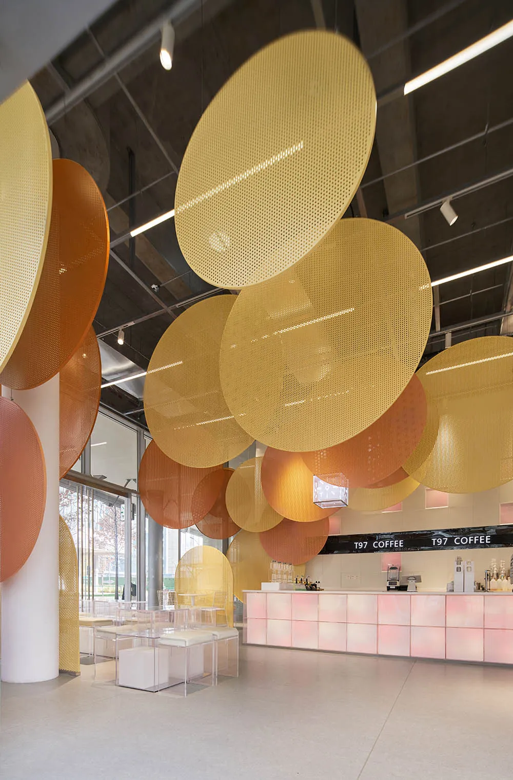 A cozy coffee shop interior features metallic perforated disks hanging from the ceiling.