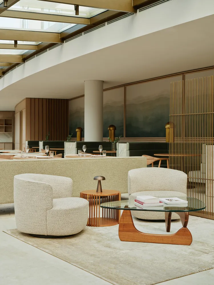 A modern restaurant interior featuring minimalist design elements, with wooden chairs, fabric seating, and glass coffee table