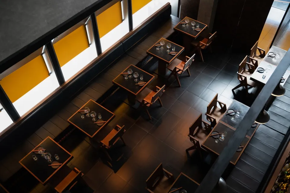Modern restaurant interior with wooden flooring, square tables, and minimalist design.