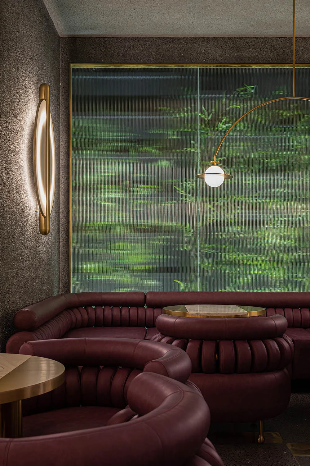 Modern interior design featuring curved leather sofas in front of a large, textured glass window showcasing green foliage.