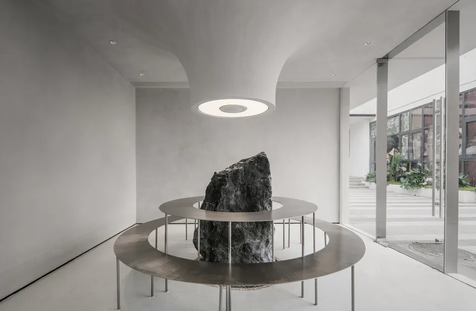 A minimalist lounge area with a metal base structure and a central stone feature.