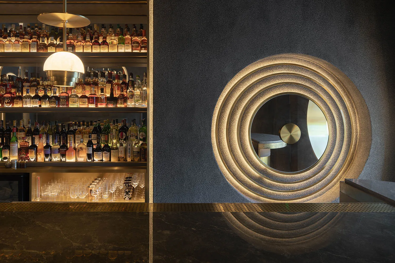 A modern bar featuring a concrete counter with a circular perforated detail and illuminated shelves.