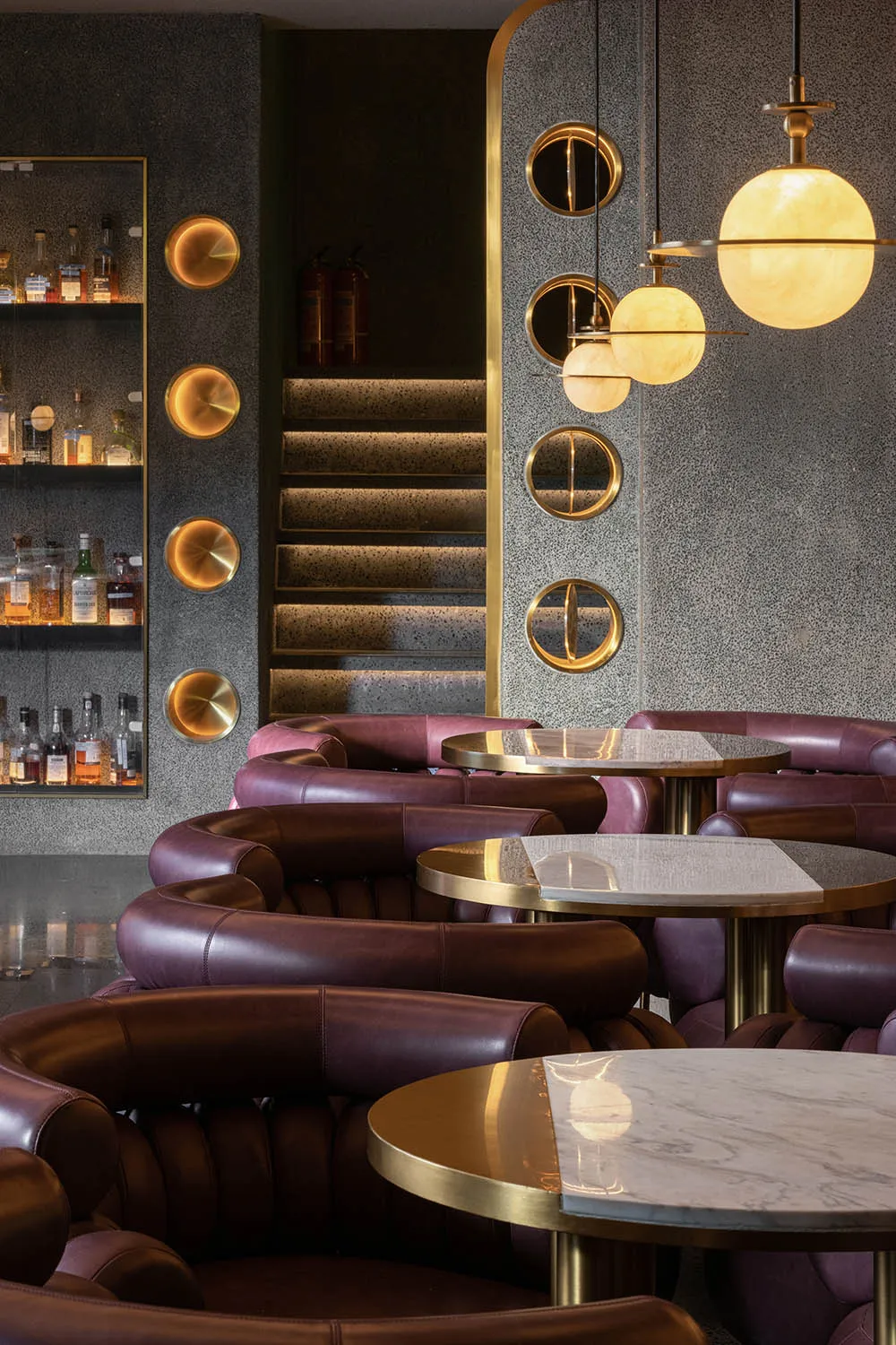 Interior design of a modern restaurant bar featuring leather seating, marble tables, and glass pendant lights.