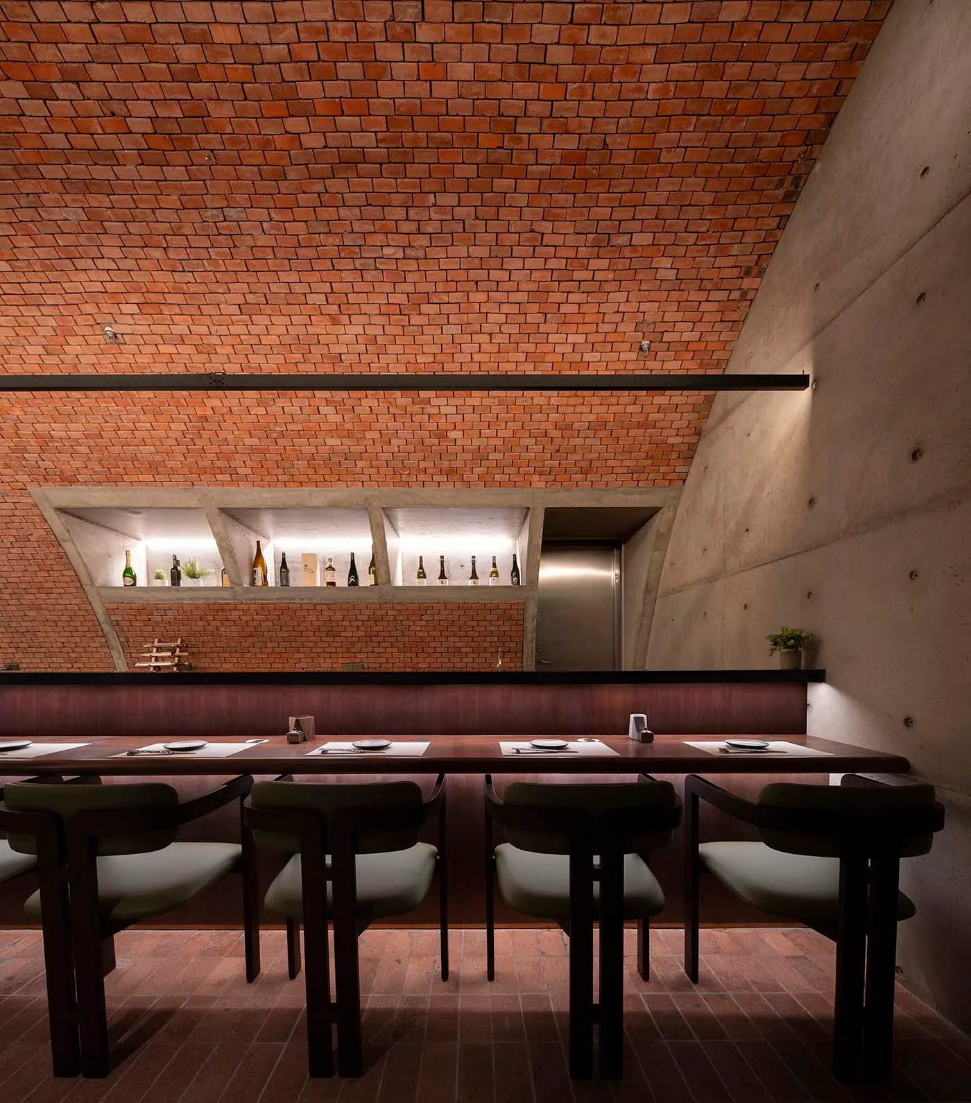 Industrial style restaurant interior with exposed brick ceiling, concrete walls, and a polished wooden table with place setti
