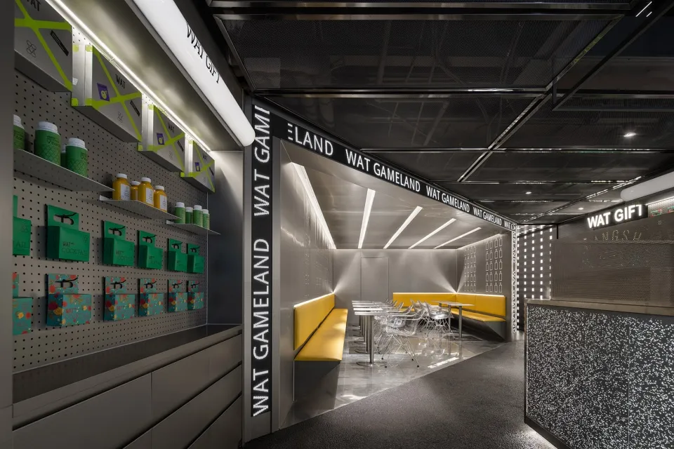 Modern restaurant interior featuring black metal and glass elements, yellow seating areas, and illuminated signage.
