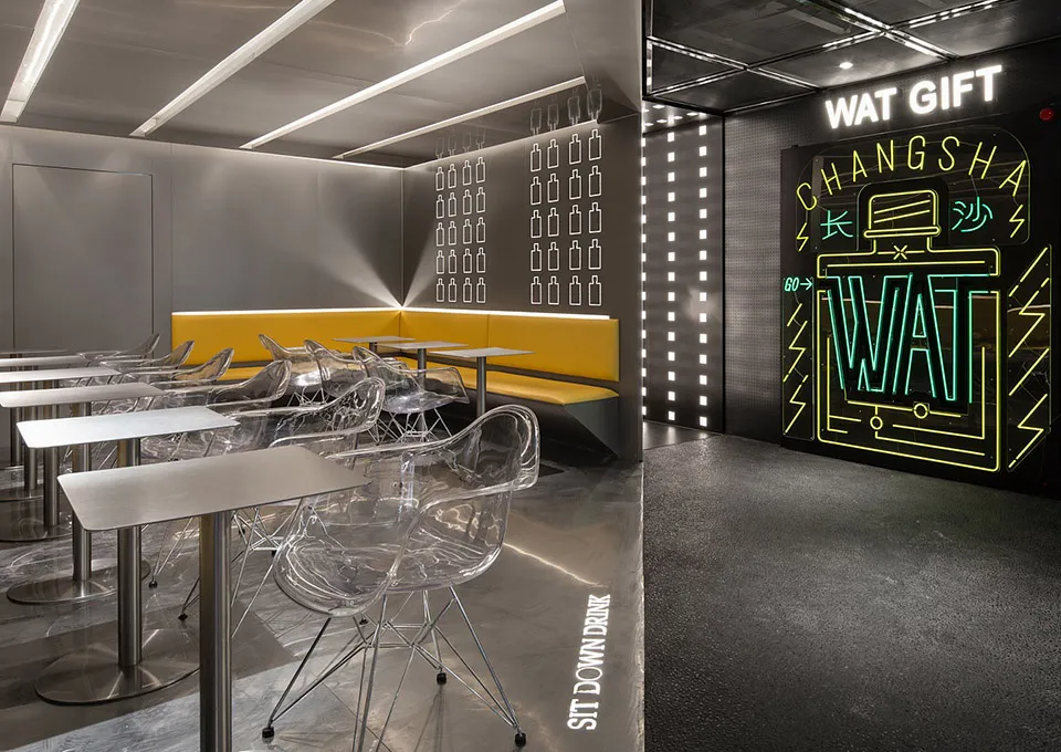 A modern restaurant interior with metallic tables and chairs, a yellow bench, and a neon sign that reads 'WAT GIFT CHANGSHA'.