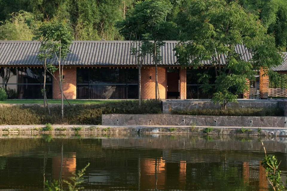 一座擁有紅磚牆與黏土屋瓦的現代住宅建築,倒映在寧靜的湖面上。