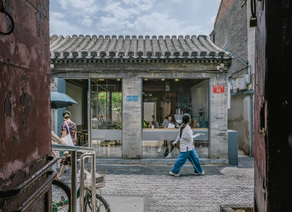 A coffee shop exterior made of clay brick, with people walking by and a sign that says Voyage Coffee.