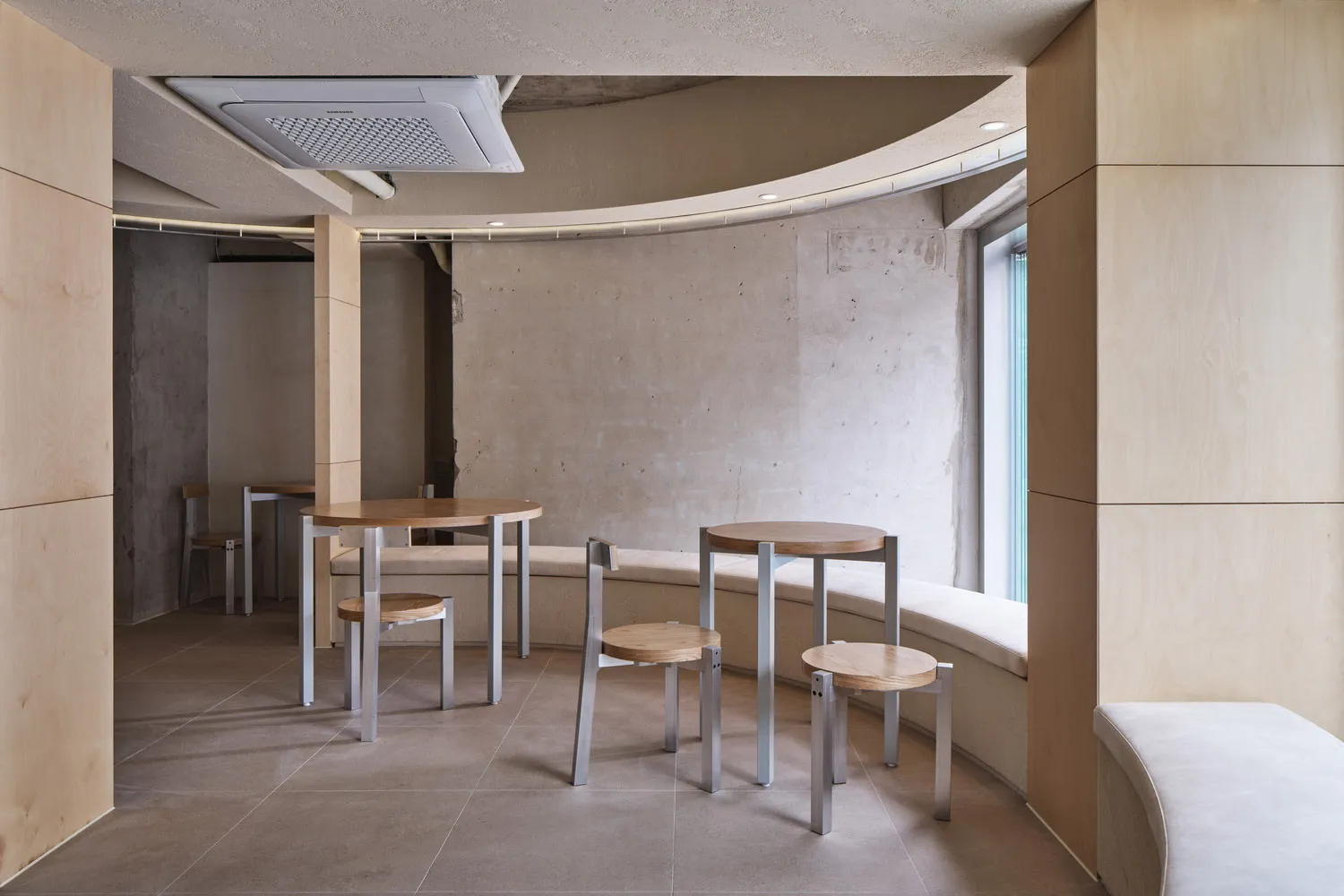 A modern cafe interior featuring wooden furniture, concrete walls, and metallic accents.