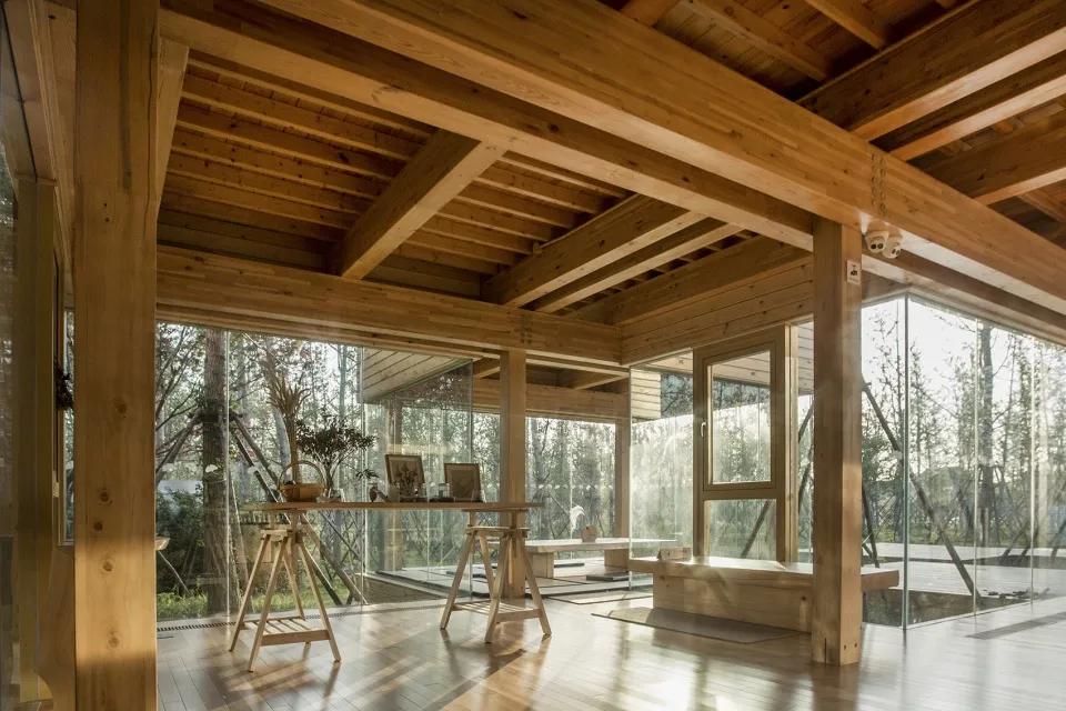 A modern living room with wooden floors and walls, featuring a large glass window and a wooden table with chairs.