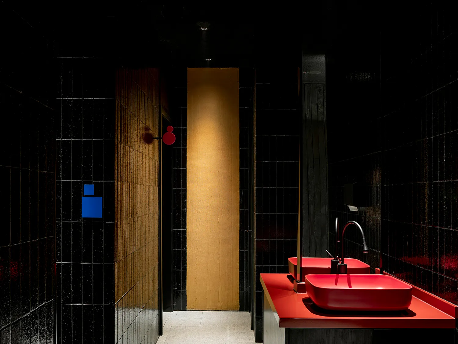 Modern restroom with sleek black tiles and vibrant red countertops, featuring red faucets and a unique, minimalist design.