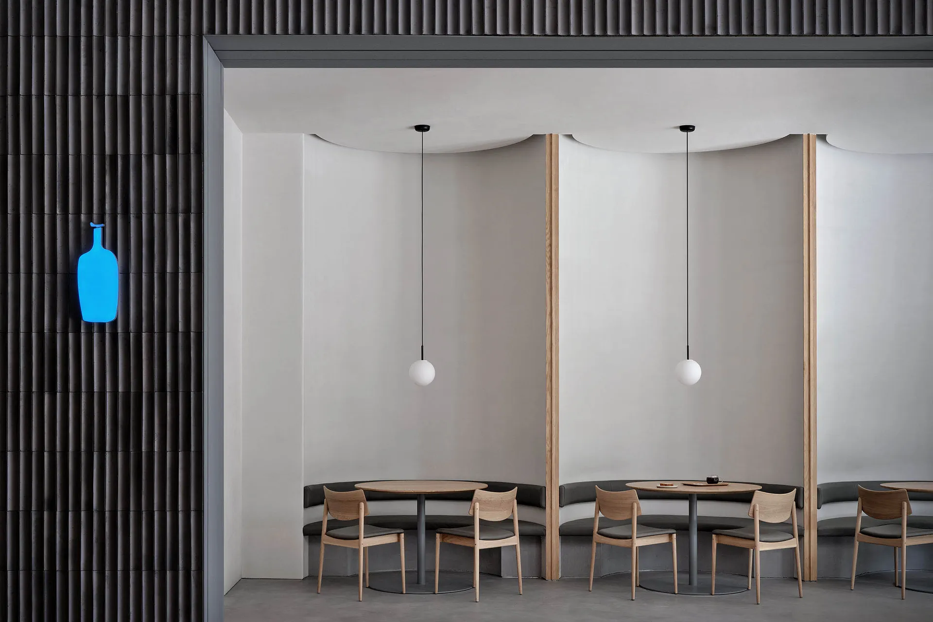 A minimalist cafe interior with concrete walls, round wooden tables, and wooden chairs.