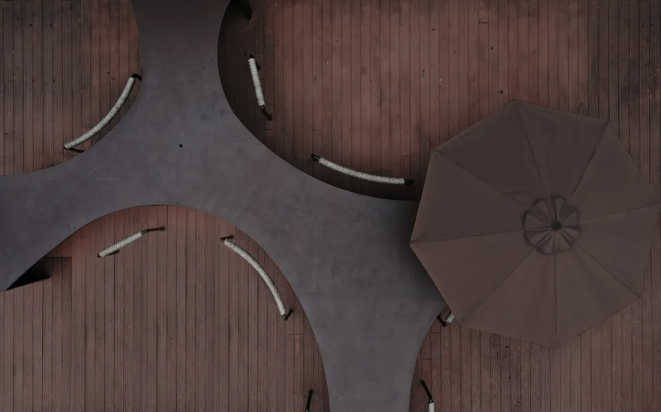 A modern outdoor lounge area featuring concrete seating and a large brown umbrella.