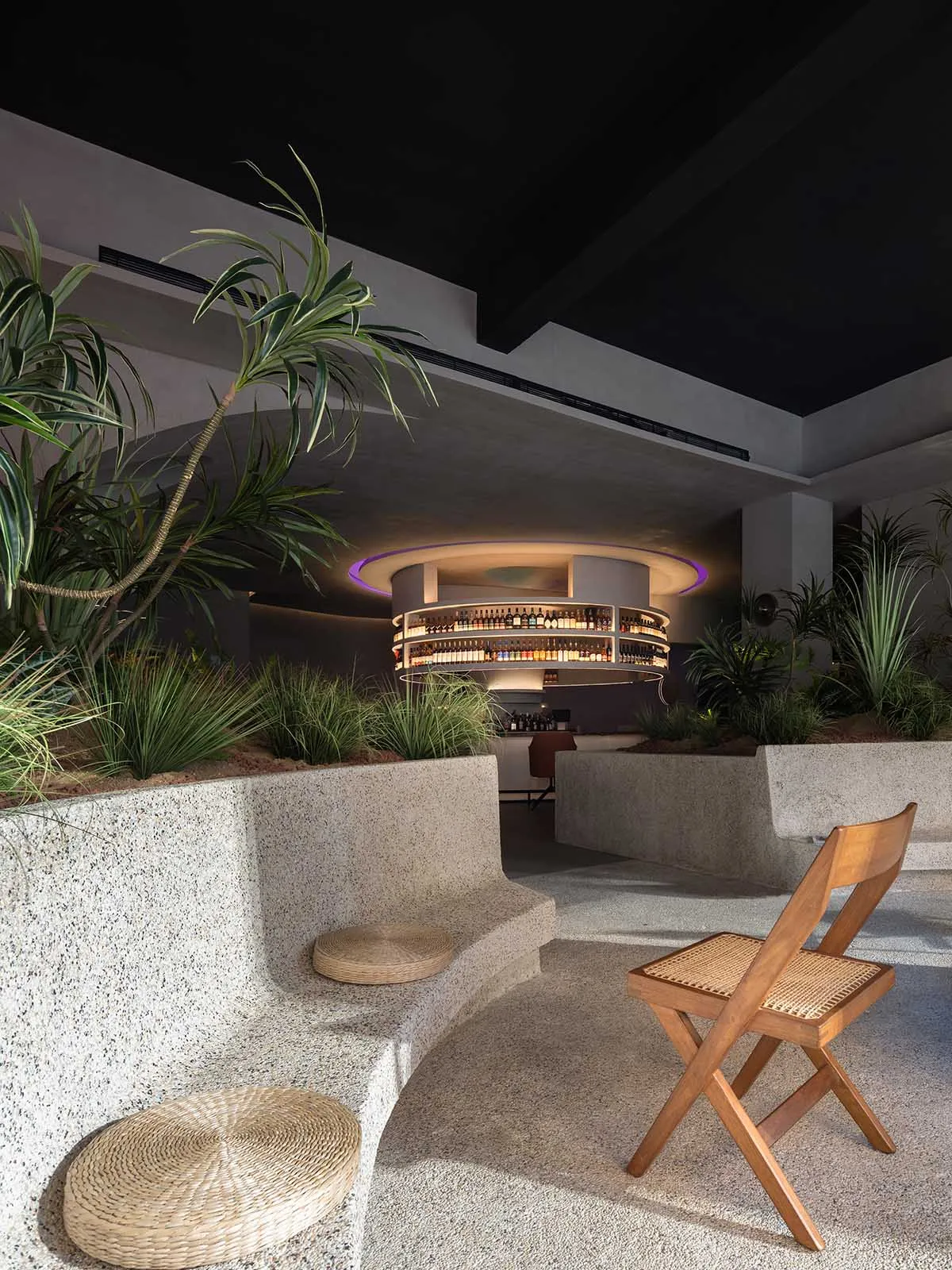 An elegant modern bar area with a circular bar counter, concrete seating, and lush greenery.