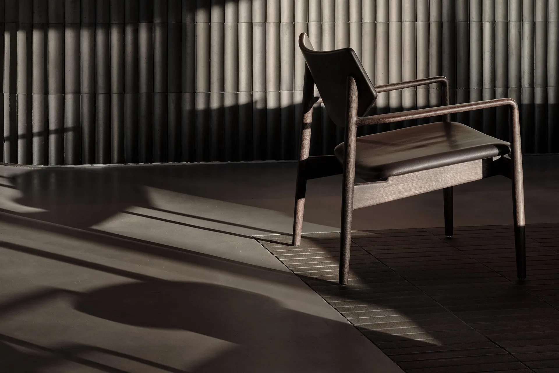 Modern chair with wooden staine in a dark, minimalist interior setting.