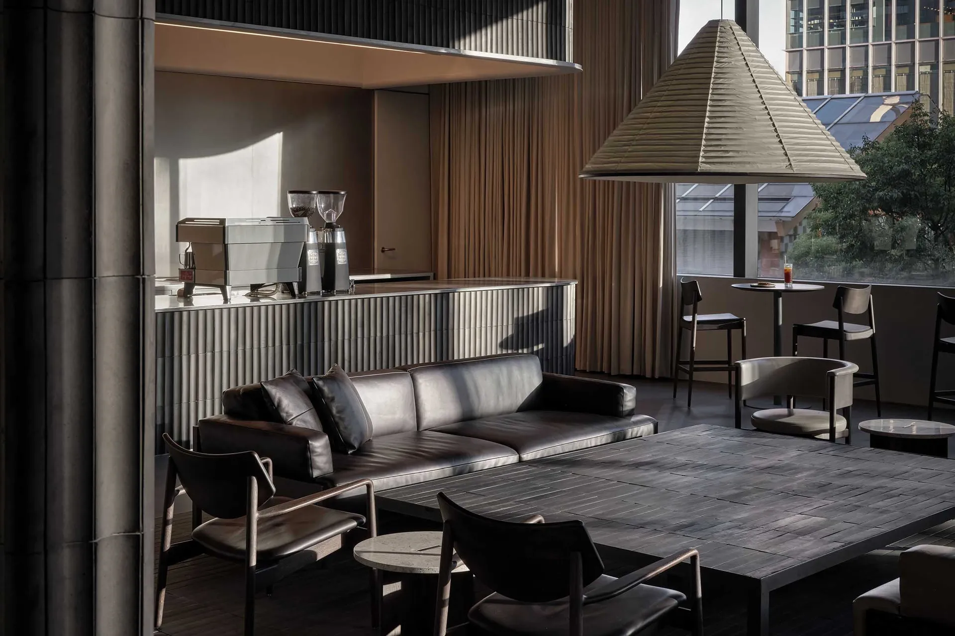 Modern coffee shop interior design featuring black leather sofas and metallic furniture against concrete walls.