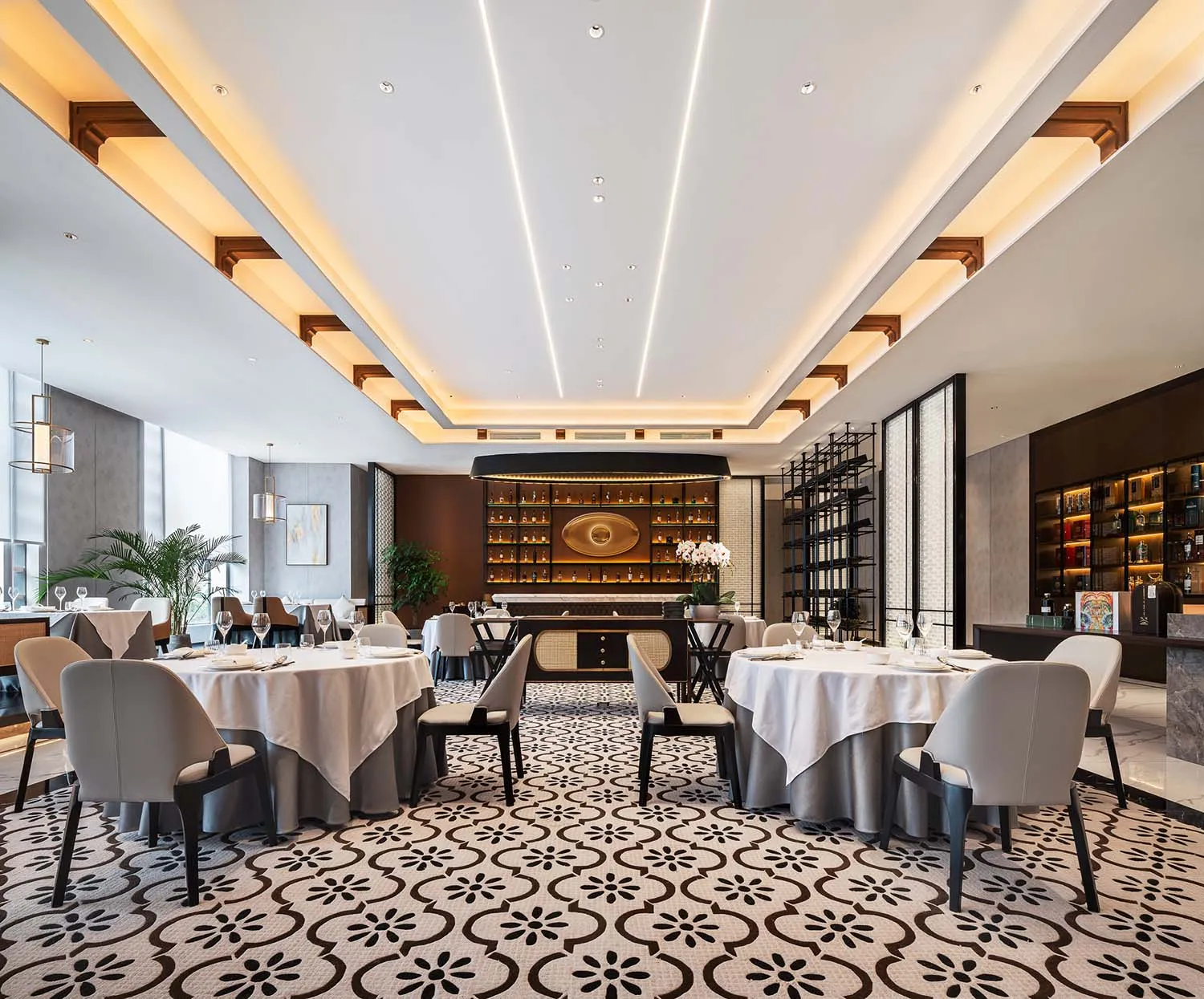 A modern restaurant interior with marble patterned floor, white tablecloths, and gray chairs.