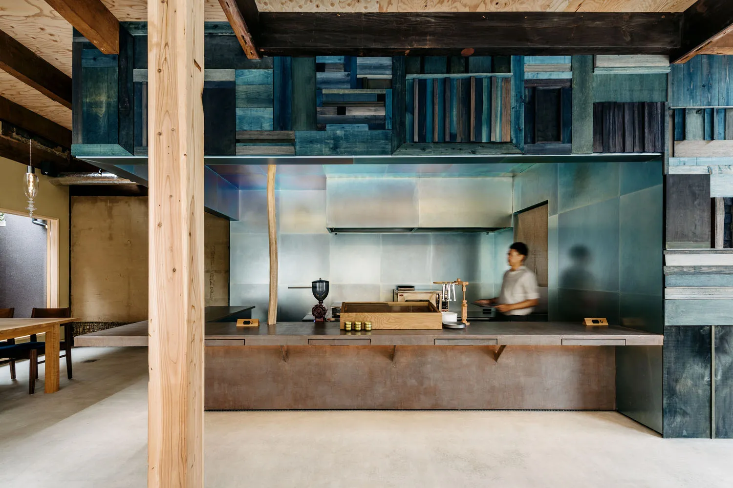 A modern kitchen with metallic and wooden surfaces and a blue-tinted glass partition.
