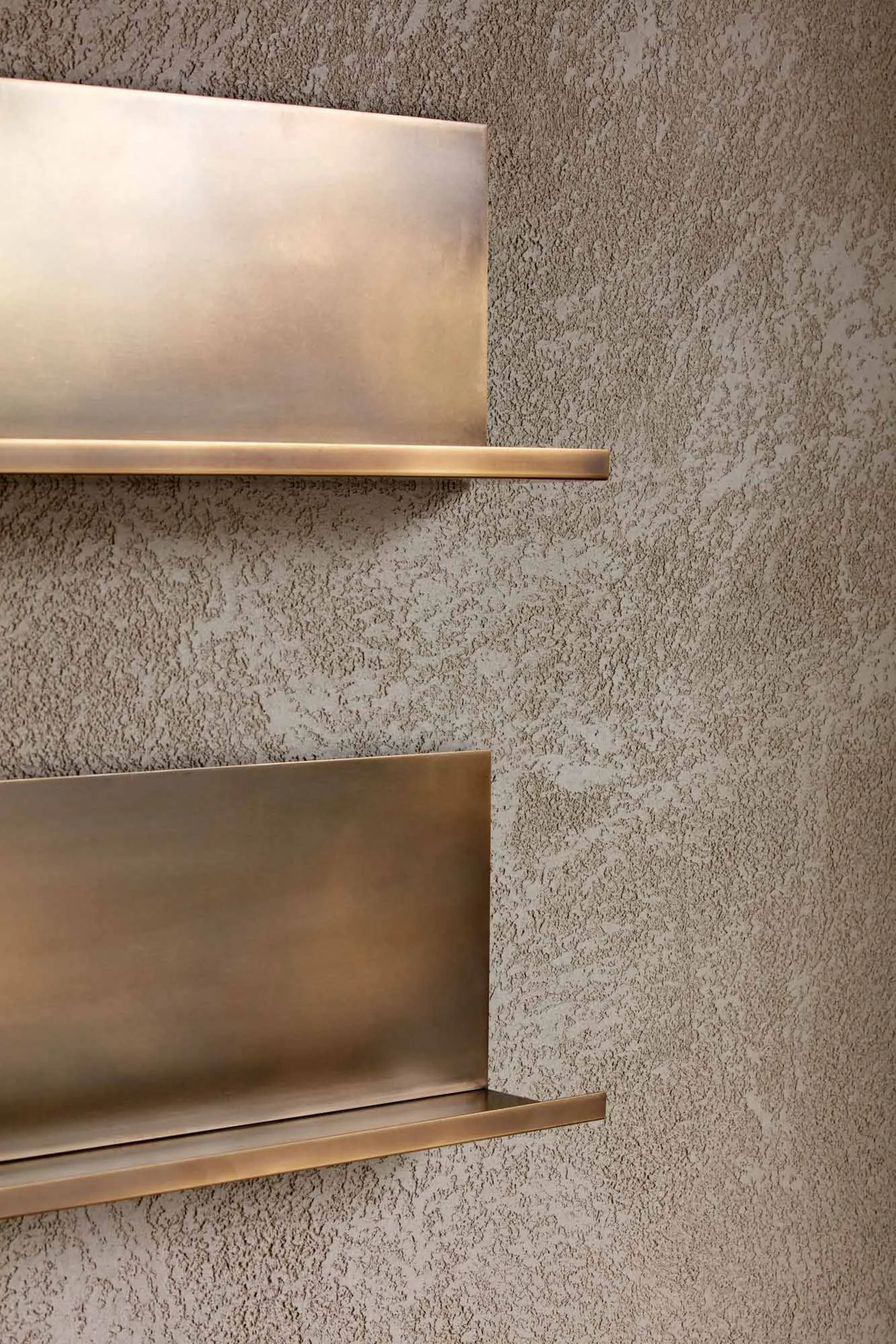 A modern, metal shelf mounted on a textured wall.